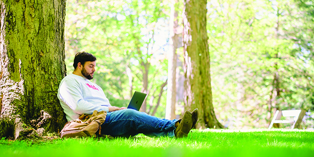 Jackson Miller sits under a tree with a laptop computer